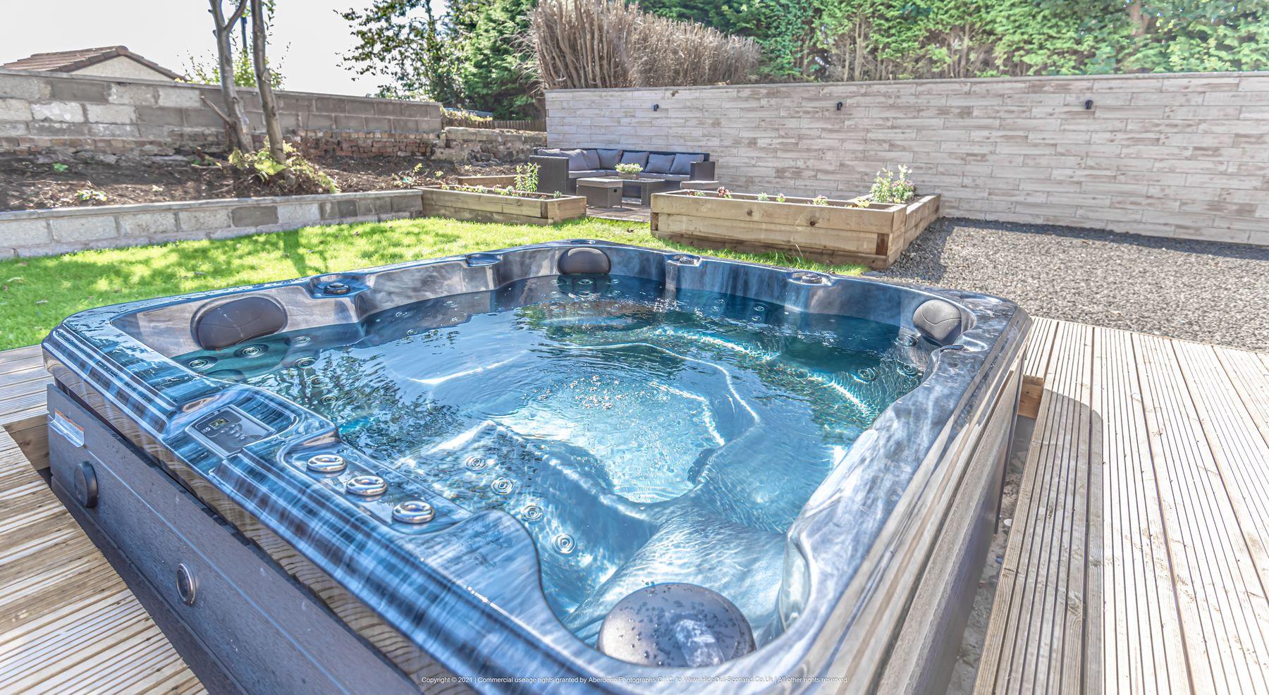 The hot tub at The HideOut, lit water on a timber deck in the walled garden